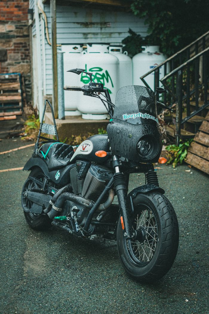 A sleek black motorcycle with unique decals parked on wet pavement in an urban setting.